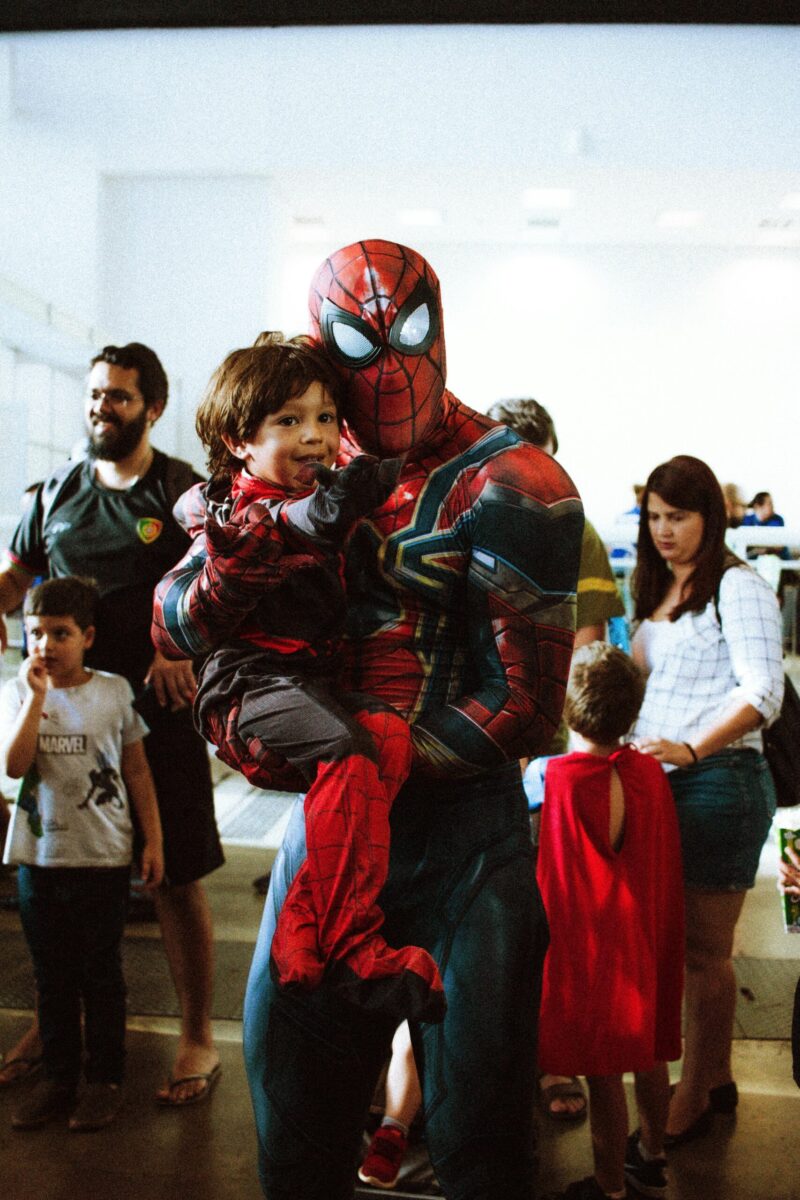 Spider-Man cosplayer lifting a young fan, capturing the joy of Comic Con.