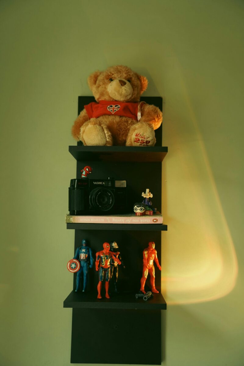 Shelf with teddy bear, vintage camera, and superhero figures, casting soft shadows.